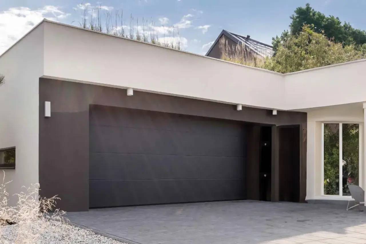 Façade moderne d'un garage double avec porte sombre, entourée d'un jardin minimaliste.