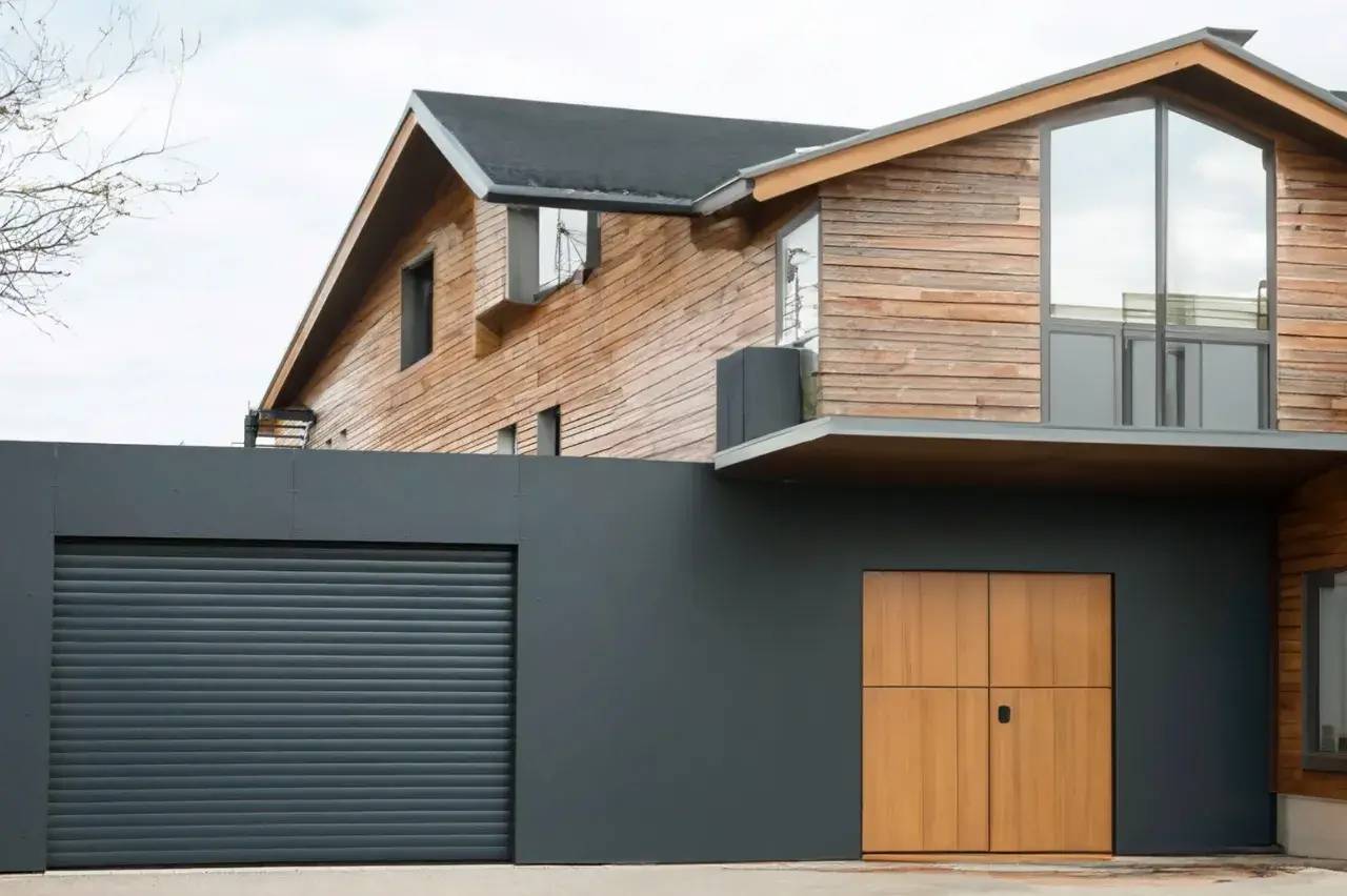 Maison moderne en bois avec une façade en métal noir et une porte de garage grise.