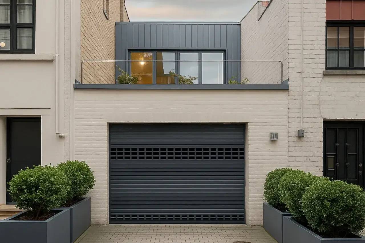 Façade moderne en briques blanches avec un garage gris et une terrasse à l'étage, entourée de plantes en pots.