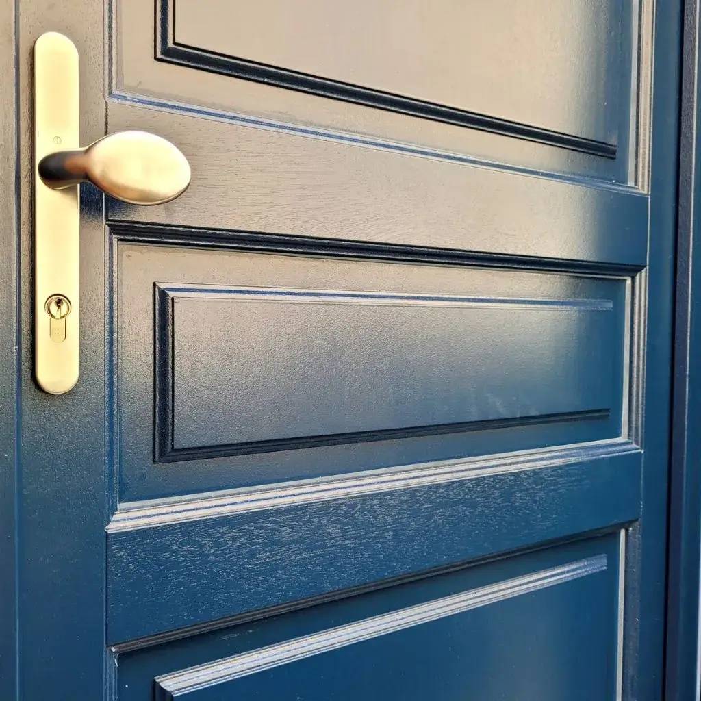 Cette image montre une porte en bois bleu foncé avec une poignée métallique dorée.