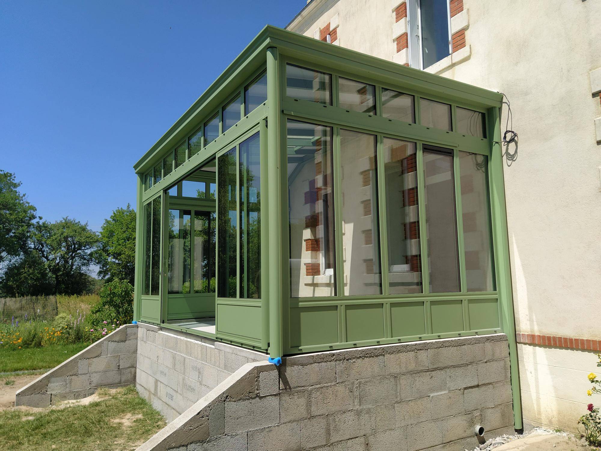 Véranda en aluminium verte ajoutée à une maison de campagne