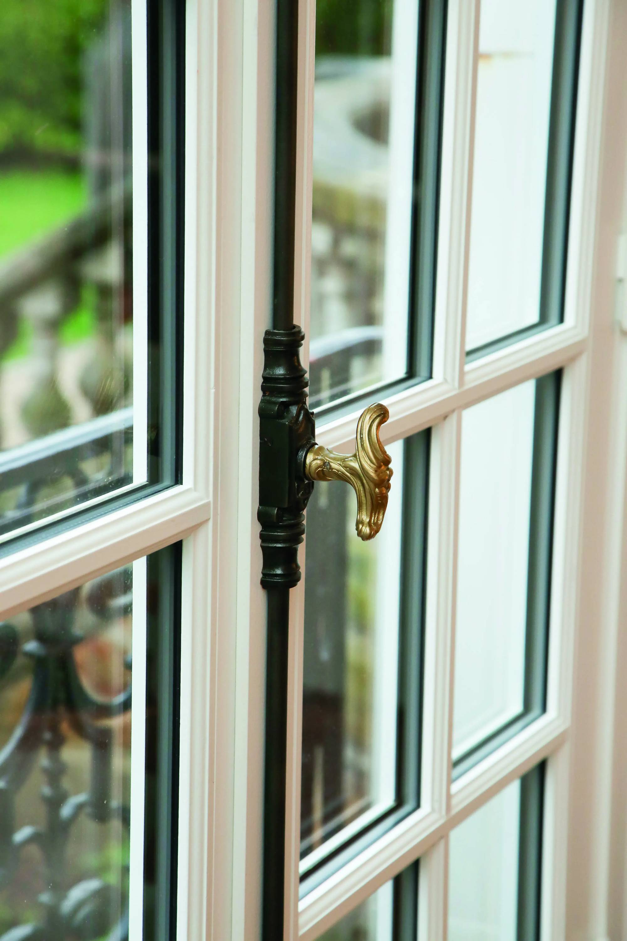 Fenêtre en bois blanc à double vitrage avec poignée en laiton doré et vue floue sur un jardin en arrière-plan.